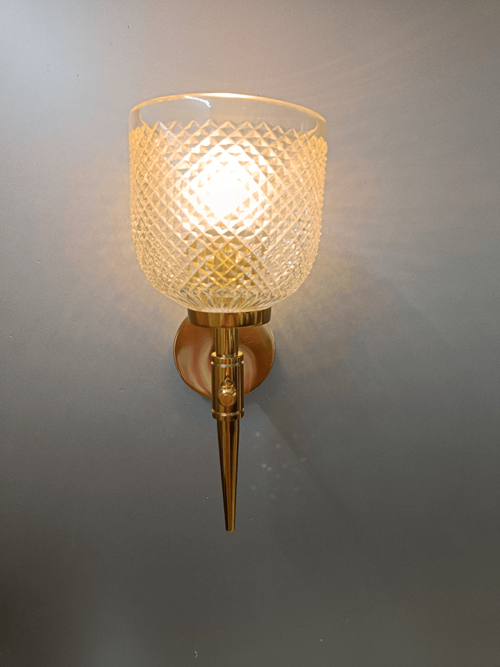 Wall lamp with gold PVD finish and clear, diamond-cut crystal glass, ideal for bedrooms.