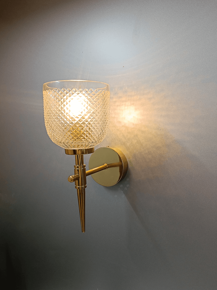 Diamond-cut crystal glass and a gold PVD finish make this wall lamp a luxurious addition to any bedroom.