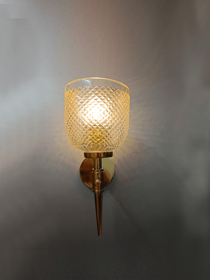 Crystal clear glass wall lamp with gold PVD finish, ideal for bedroom lighting.