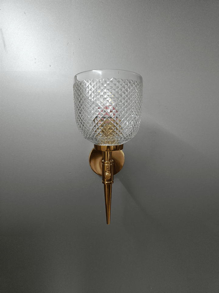 Bedroom wall lamp with gold PVD finish and diamond-cut crystalline glass.