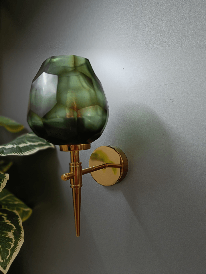 Stunning gold wall sconce boasting an uneven, diamond-cut dark green glass shade.