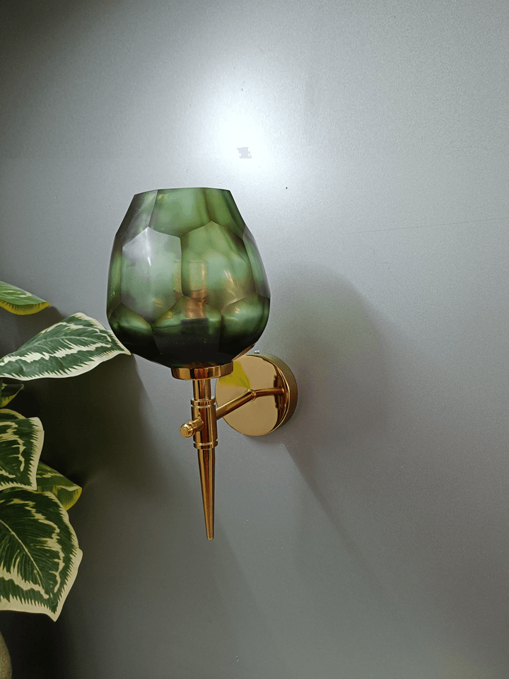 Unique gold PVD wall light design with an asymmetrical dark green, diamond-cut glass shade.