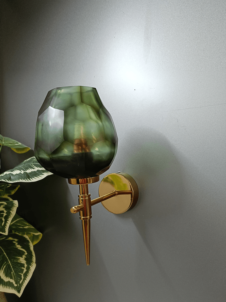 Modern wall lamp with a luxurious gold PVD finish and an uneven, dark green diamond-cut glass.