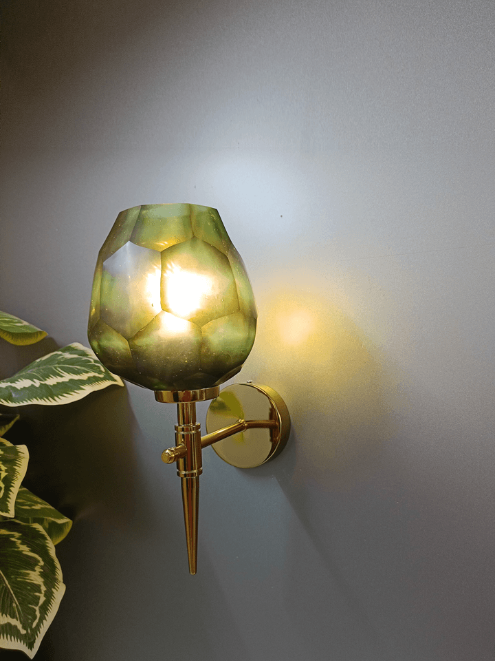 Eye-catching gold PVD wall light design featuring a dark green, diamond-cut glass shade with an uneven form.