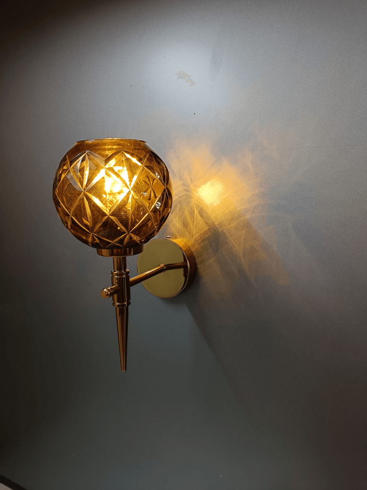 Illuminate your bedroom in style with this gold PVD wall sconce and its captivating amber crystal glass shade (India).