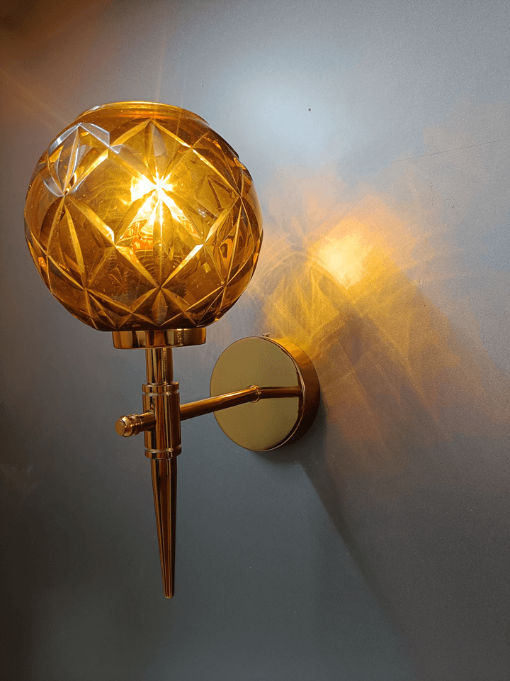 Gold PVD wall sconce with amber crystal glass, hand-cut for a dazzling display in the bedroom (India).