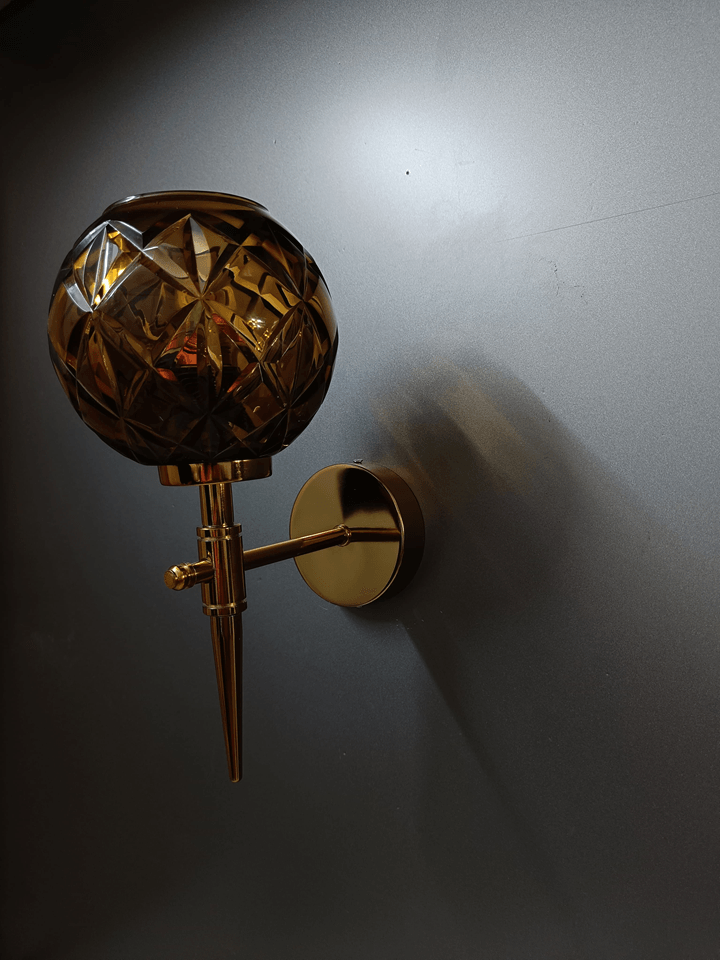 Modern wall sconce featuring a gold PVD finish and hand-cut amber crystal glass for a touch of elegance in your bedroom (India).