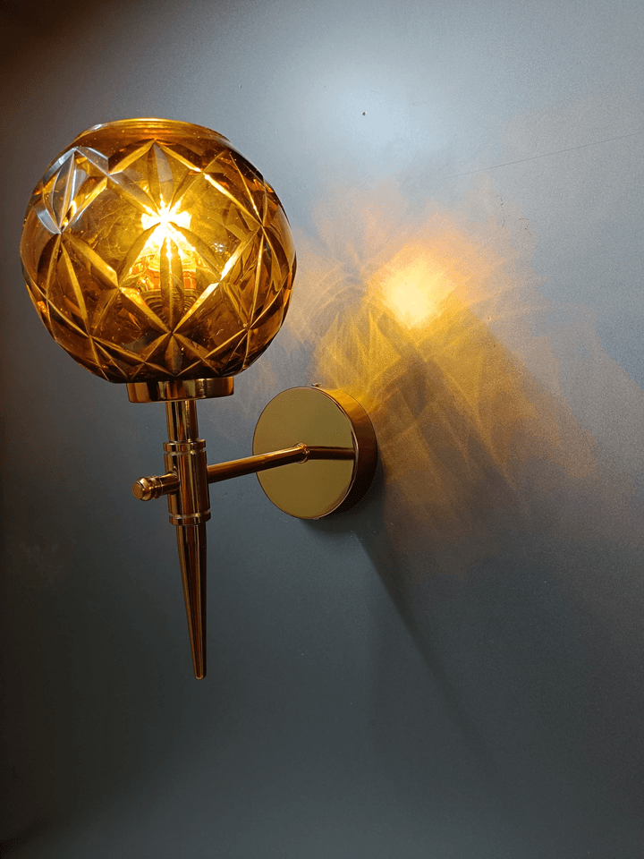 This gold PVD wall sconce with amber crystal glass adds a touch of luxury to your bedroom decor (India).