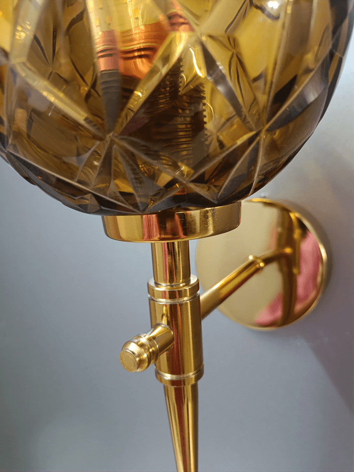 Elegant gold PVD wall sconce featuring hand-cut amber crystal glass for a touch of warmth in the bedroom.