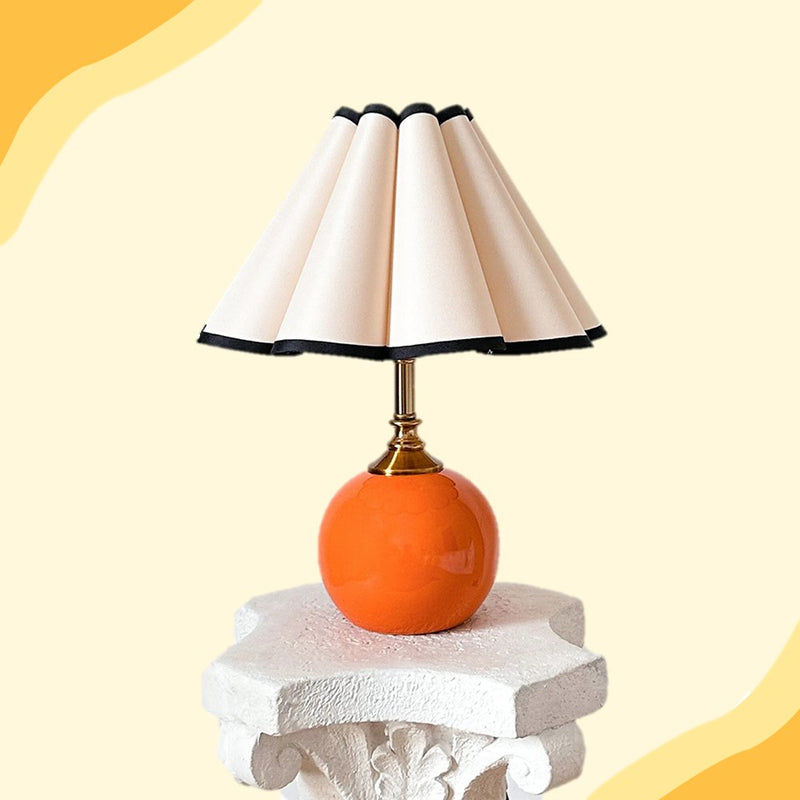 Table lamp with an orange base and white shade on a decorative pedestal against a yellow background