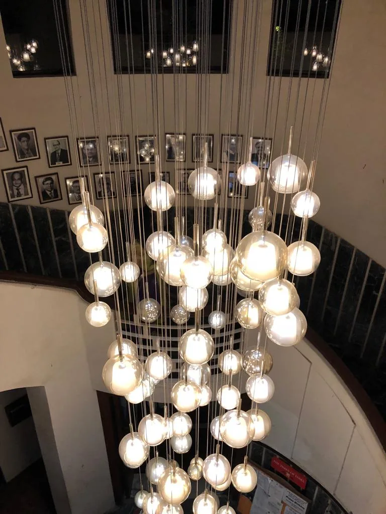Warm illuminated globe chandelier cascading through a school stairwell in Siliguri