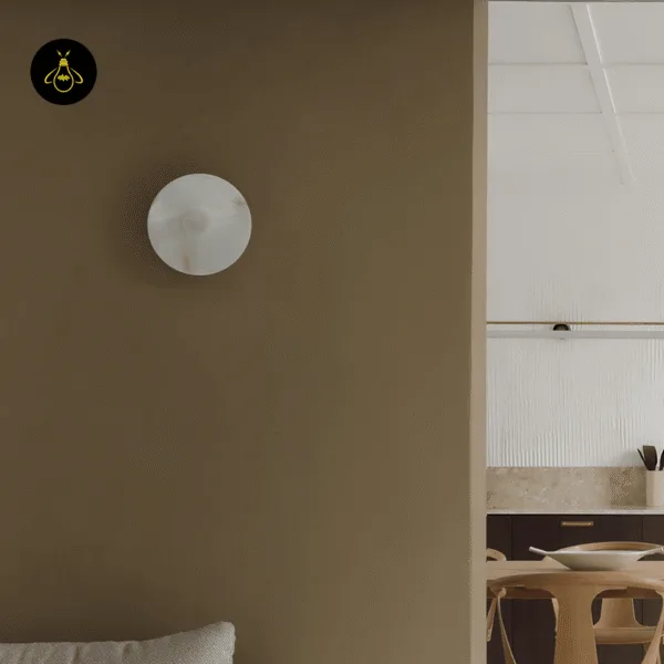 Disc wall light in white alabaster on a taupe wall beside a doorway into a dining area