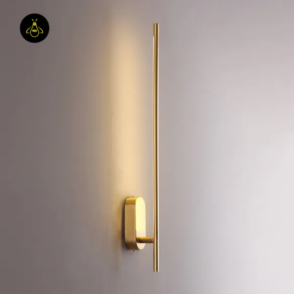 Brass wall sconce lit on a grey wall, the LED rod washing the wall with warm light above its oval backplate