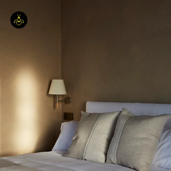 Fabric wall light above a light switch beside a white upholstered bed