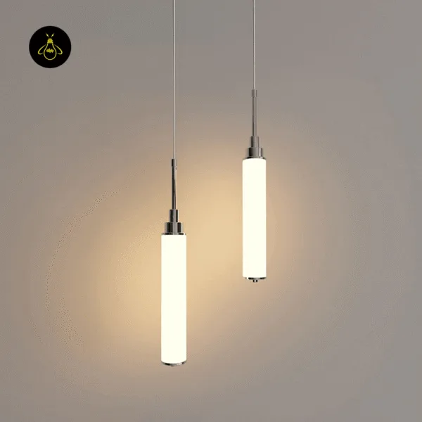 Two lit chrome cylinder pendant lights hanging at different heights against a beige wall
