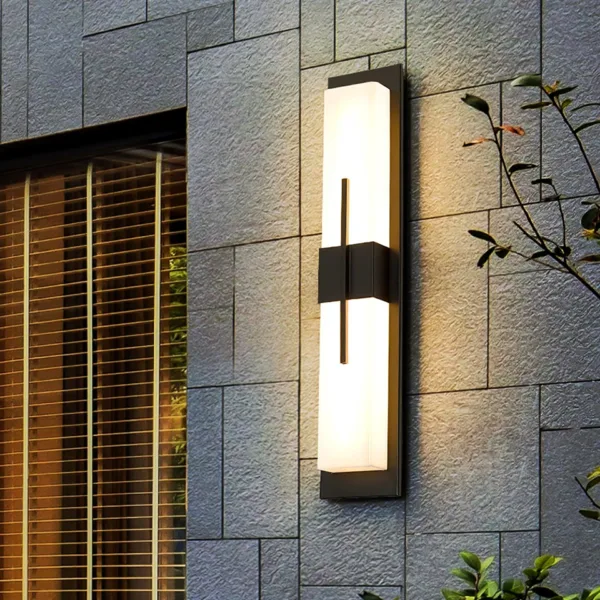 Alabaster outdoor wall light on a grey stone-clad exterior wall beside a window at dusk