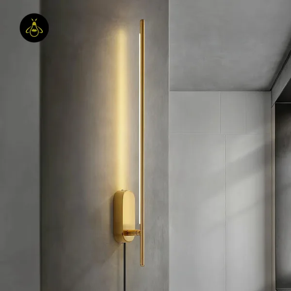 Brass wall sconce lit on a grey textured wall, showing the short arm joining the rod to the oval backplate