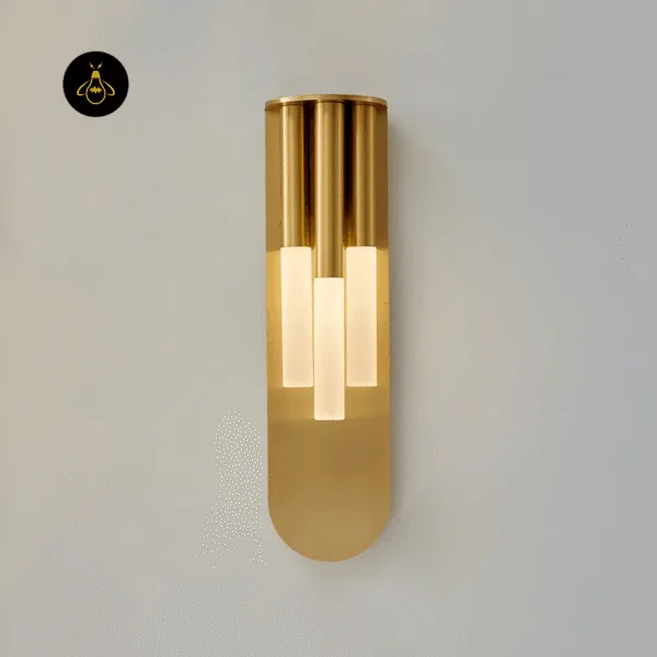 Glass wall lamp lit on a grey wall, three staggered opal glass tubes held in gold stainless steel tubes
