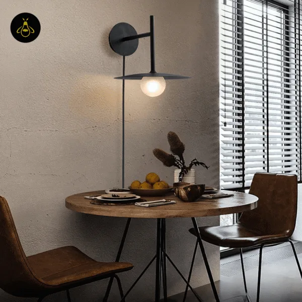 Black wall lamp glowing over a round wooden dining table by a window