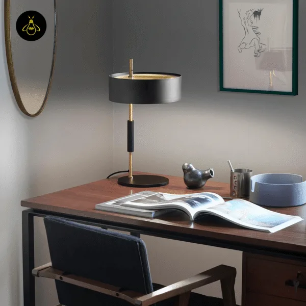 Black gold table lamp with drum shade on a walnut study desk