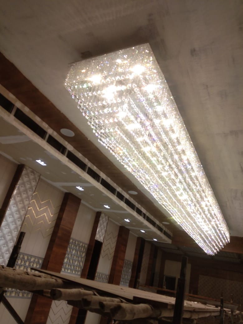 Full 24-foot length of the linear crystal chandelier glowing above the banquet hall in Pune during installation