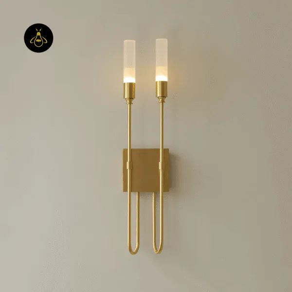 Gold wall sconce lit warm on a plain beige wall, light glowing up through two opal borosilicate glass tubes
