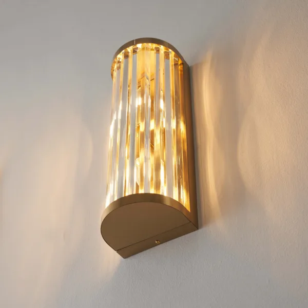 Side angle of the ribbed glass wall light, lit, showing the brushed gold half-round cap and backplate depth