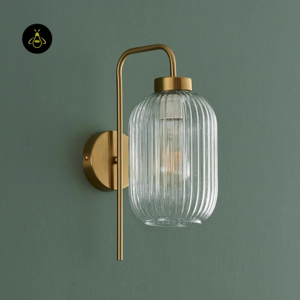 Fluted glass wall light switched off, clear ribbed borosilicate glass shade and gold cap on a green wall