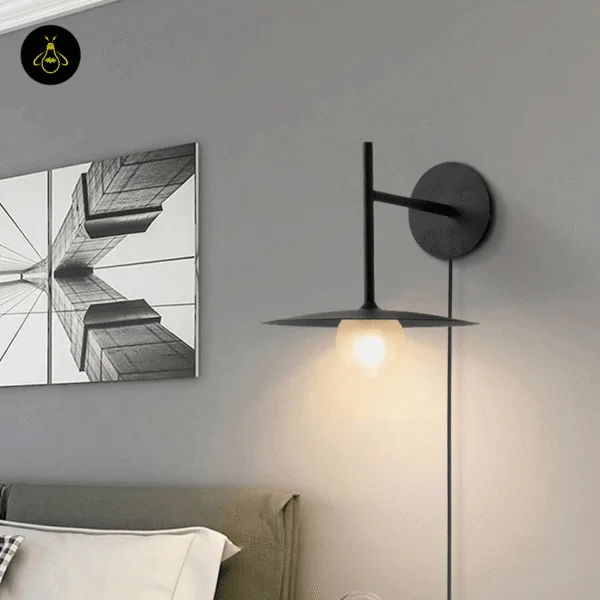 Black wall lamp lit beside a bed and an abstract photo print on a grey wall