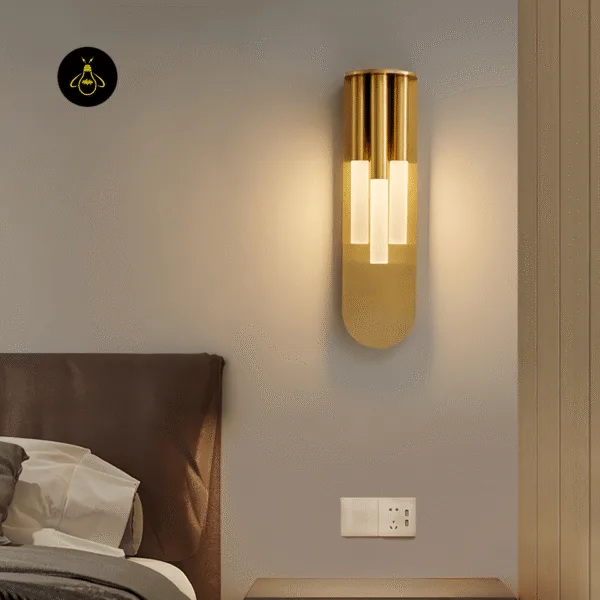Gold glass wall lamp glowing beside a bed, above a nightstand and wall socket