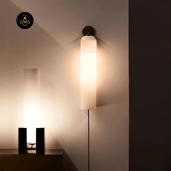 Opal borosilicate glass wall light in a dark finish glowing warm on a living room wall, cable run down the wall, beside a matching cylinder table lamp