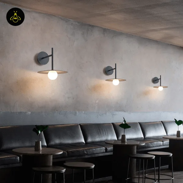 Three black wall lamps in a row along a restaurant wall above leather banquette seating
