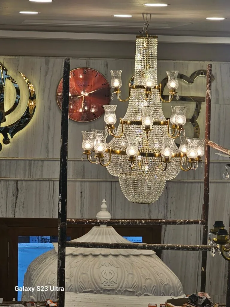 Gurudwara chandelier — gold three-tier Maharaja crystal chandelier glowing above the marble palki at Gurudwara Shri Prabhu Prem Seva Devi Saheb, Jalna