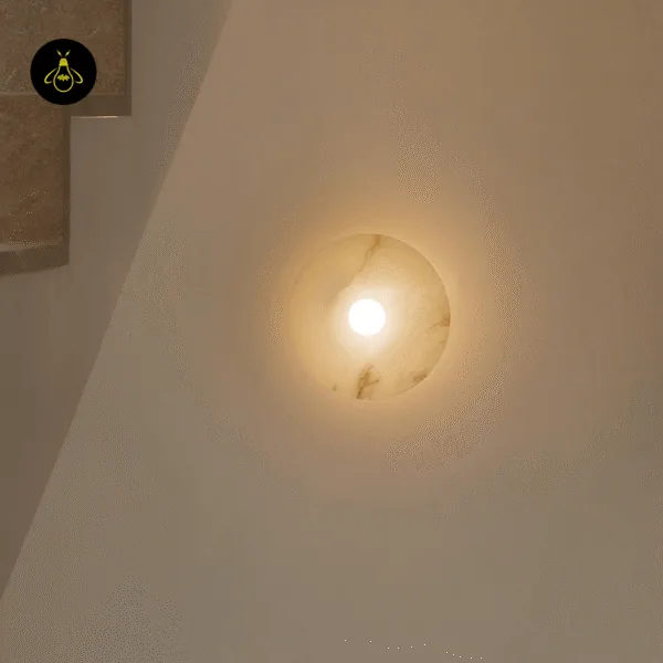 Disc wall light switched on beside a staircase, throwing a warm halo onto the wall around the alabaster