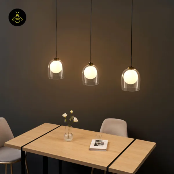 Three lit Calypso glass hanging lamps over a wooden dining table with black inlay in a dark room