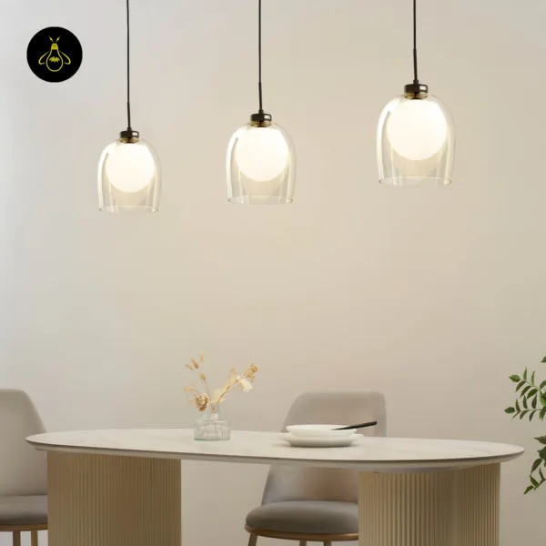 Three lit glass hanging lamps at staggered heights over an oval stone-top dining table