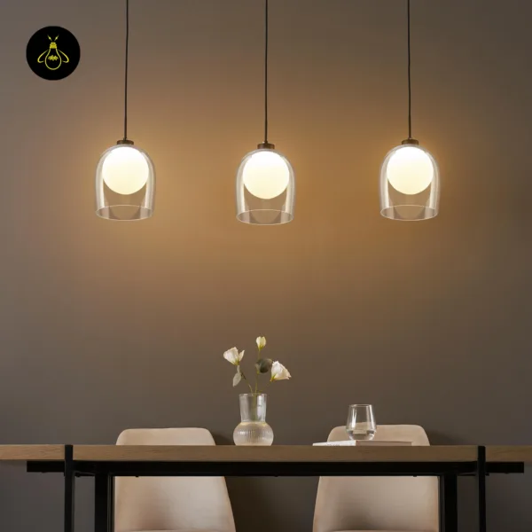 Row of three lit glass hanging lamps over a wooden dining table against a brown wall