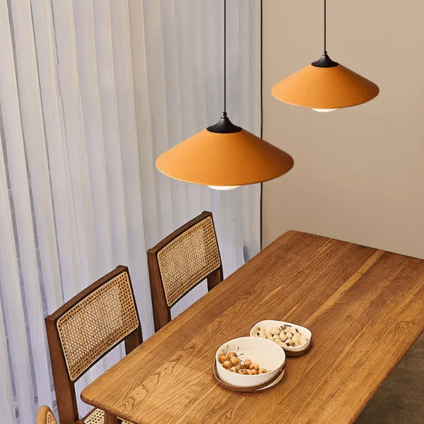 Orange conical kitchen island pendant lights hanging over a wooden dining table with cane chairs