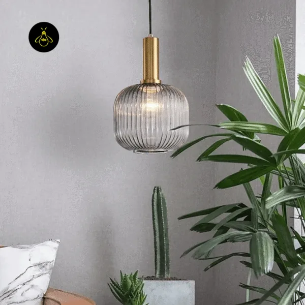 Clear fluted glass pendant light lit in a living room corner beside tall green plants and a sofa