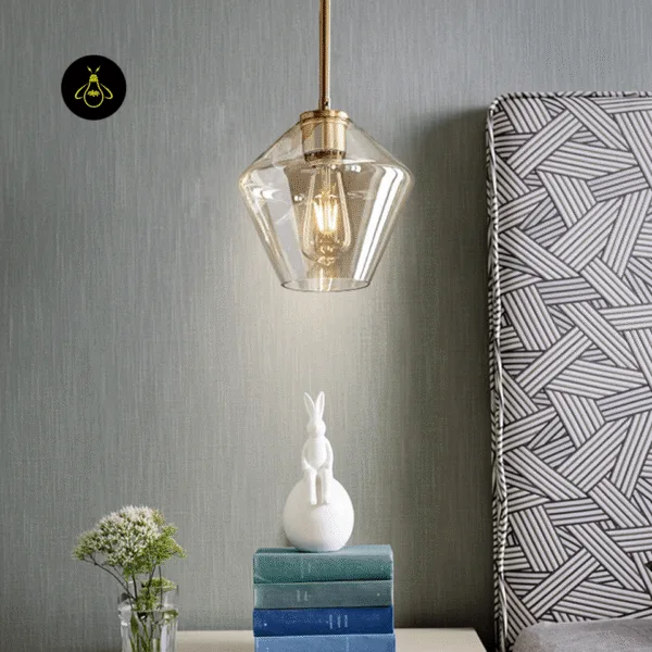 Amber glass pendant light size B glowing beside a bed above a stack of books