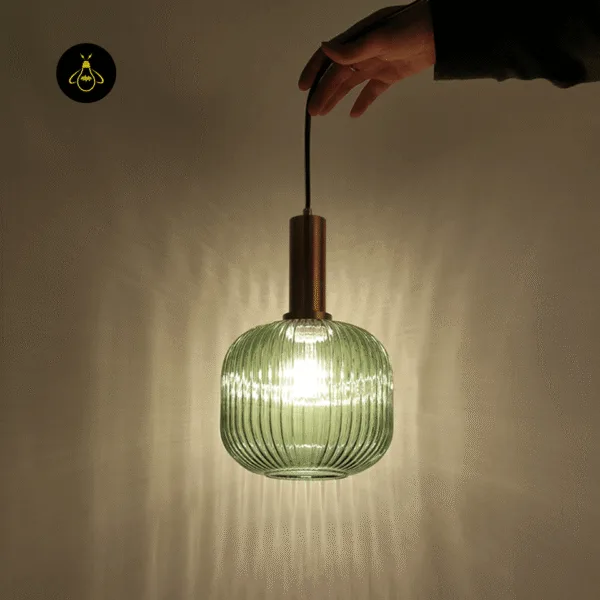 Green fluted glass pendant light switched on, the ribbed borosilicate glass throwing vertical lines of light on the wall