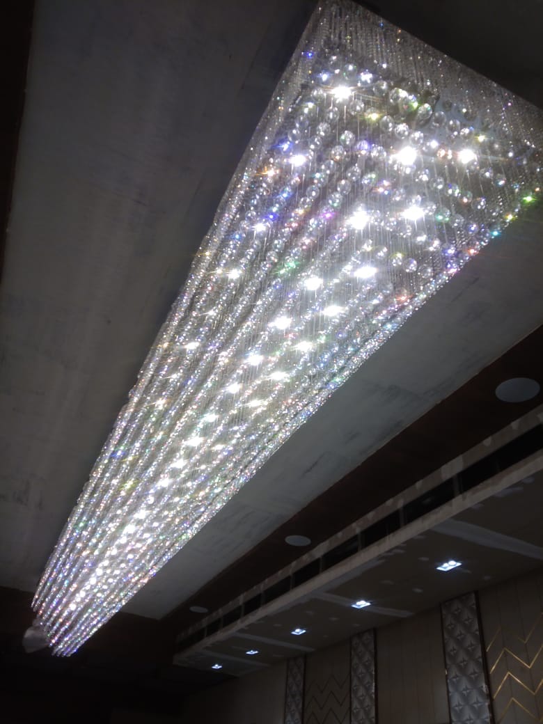 JagMag Lights team installation view of the long crystal slab chandelier sparkling with rainbow light in the Pune banquet hall