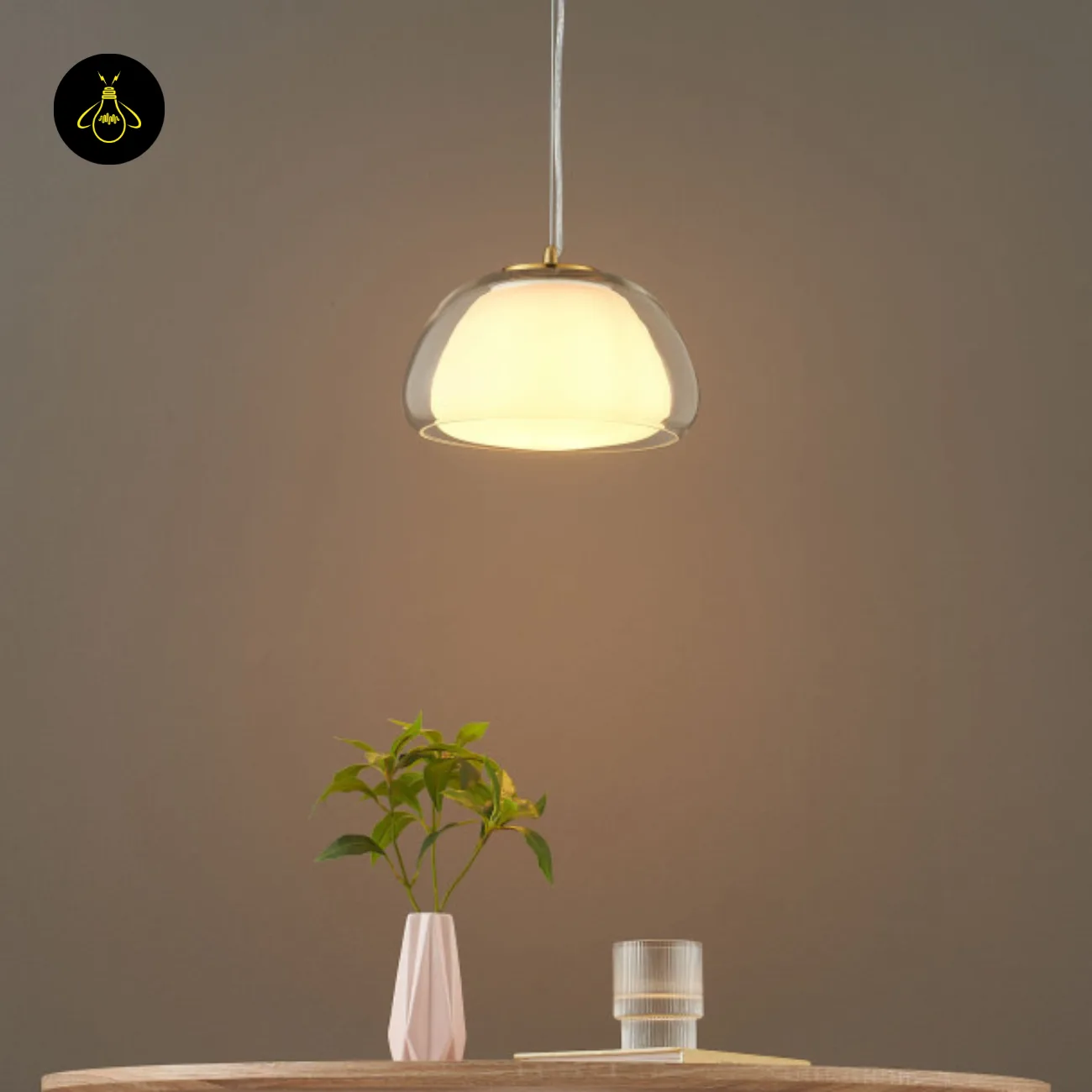 Double Glass Pendant Light – Lomelia 25 cm Dome, Gold Finish 9 Lomelia double glass pendant light lit above a wooden table with a white vase and fluted glass, front view