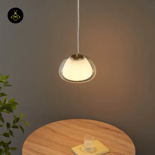 Lomelia double glass pendant light glowing warm over a round wooden dining table with a book and glass