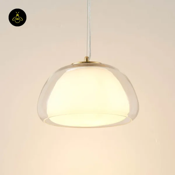 Lomelia double glass pendant light lit against a cream wall, opal inner glass glowing inside the clear champagne-tinted outer dome on a transparent cord