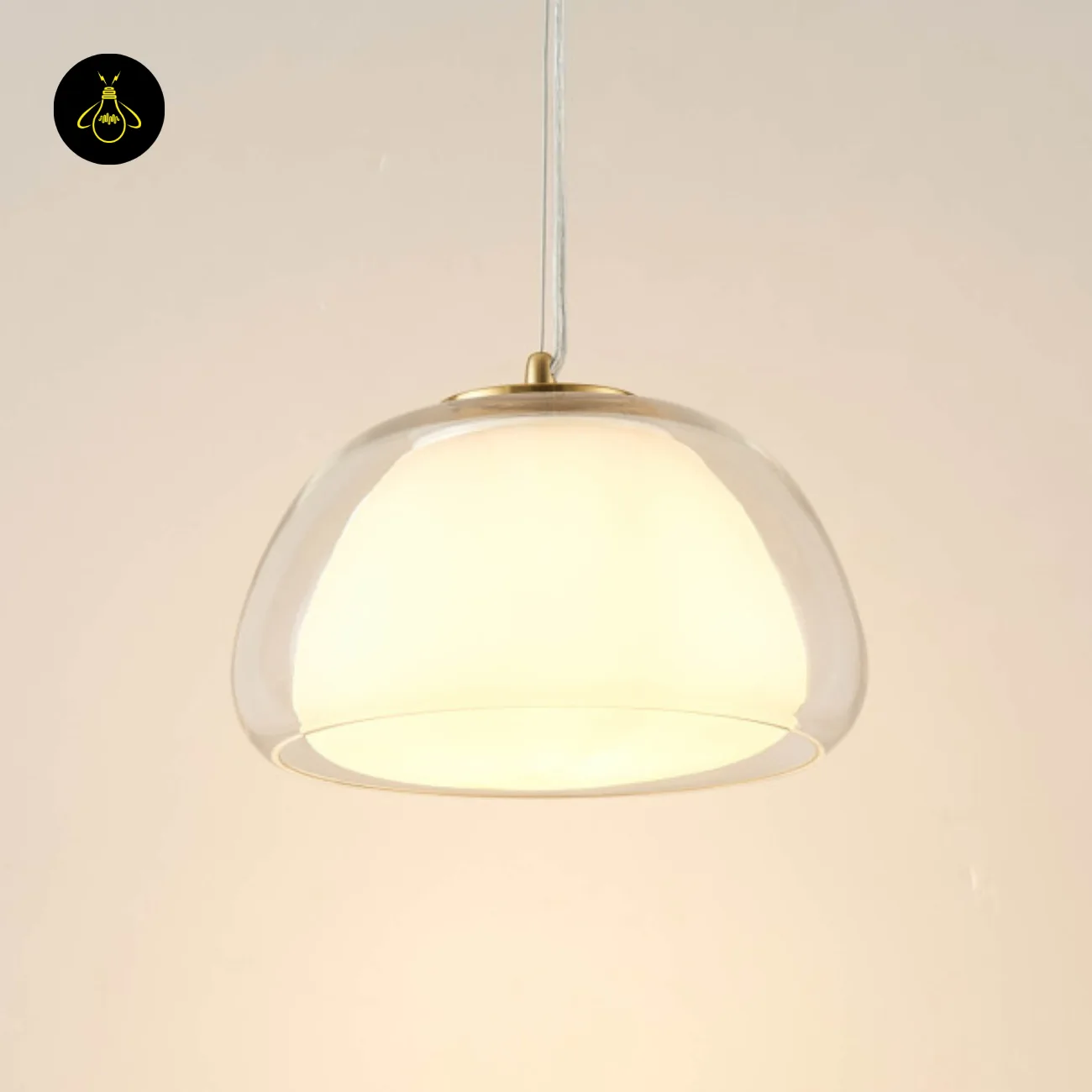 Double Glass Pendant Light – Lomelia 25 cm Dome, Gold Finish 4 Lomelia double glass pendant light lit against a cream wall, opal inner glass glowing inside the clear champagne-tinted outer dome on a transparent cord