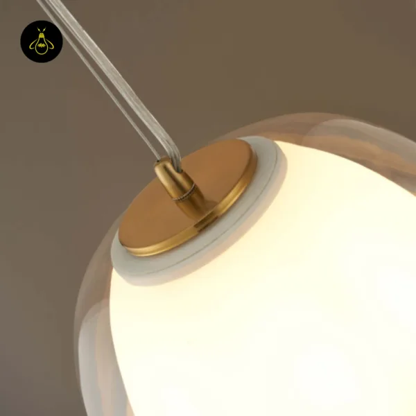 Close-up of the Lomelia double glass pendant light cap, gold-finish 304 stainless steel disc and transparent cord on the opal and clear glass domes