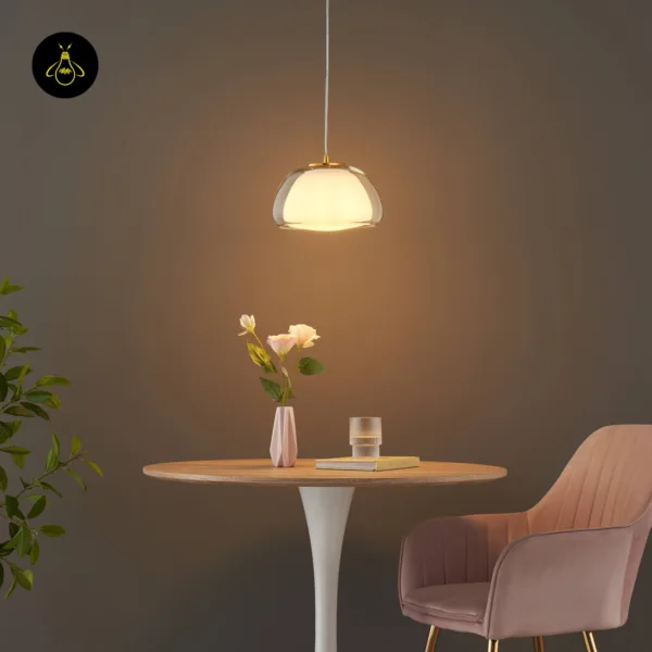 Lomelia double glass pendant light lit over a round table with white flowers and a pink armchair, warm glow on the wall