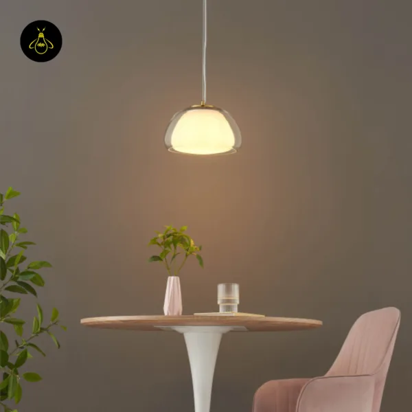 Lomelia double glass pendant light hanging over a round table beside a plant and pink armchair, soft warm light