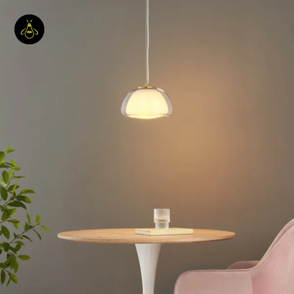 Lomelia double glass pendant light lit above a round wood-top table, opal inner shade inside the clear dome